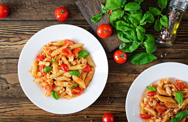 istock Penne pasta in tomato sauce with chicken, tomatoes, decorated with basil on a wooden table. Italian food. Pasta Bolognese. Top view 955920794