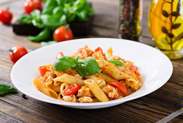 istock Penne pasta in tomato sauce with chicken, tomatoes, decorated with basil on a wooden table. Italian food. Pasta Bolognese. 955920800
