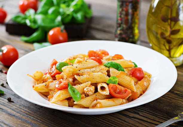 istock Penne pasta in tomato sauce with chicken, tomatoes, decorated with basil on a wooden table. Italian food. Pasta Bolognese. 955920802