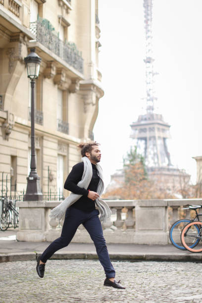 istock Afro american guy running with Eiffel Tower in background, wearing grey scarf and black sweater 955921778
