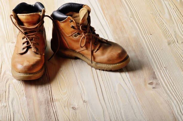 istock Yellow leather used work boots on wooden background closeup. Place for text 955921894