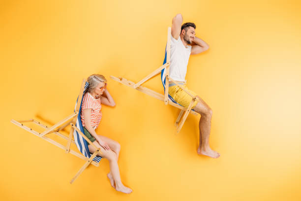 happy young couple resting in beach chairs on yellow, summer vacation concept happy young couple resting in beach chairs on yellow, summer vacation concept chaise longue woman stock pictures, royalty-free photos & images