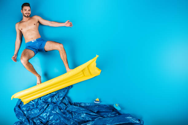 Athletic man riding a surfboard. Summer sport activity. Surfer movements on blue studio background.