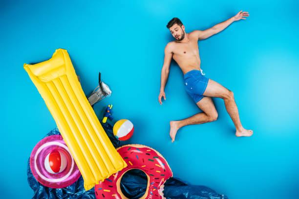 istock young man in shorts looking at beach items on blue, summer vacation concept 955932832