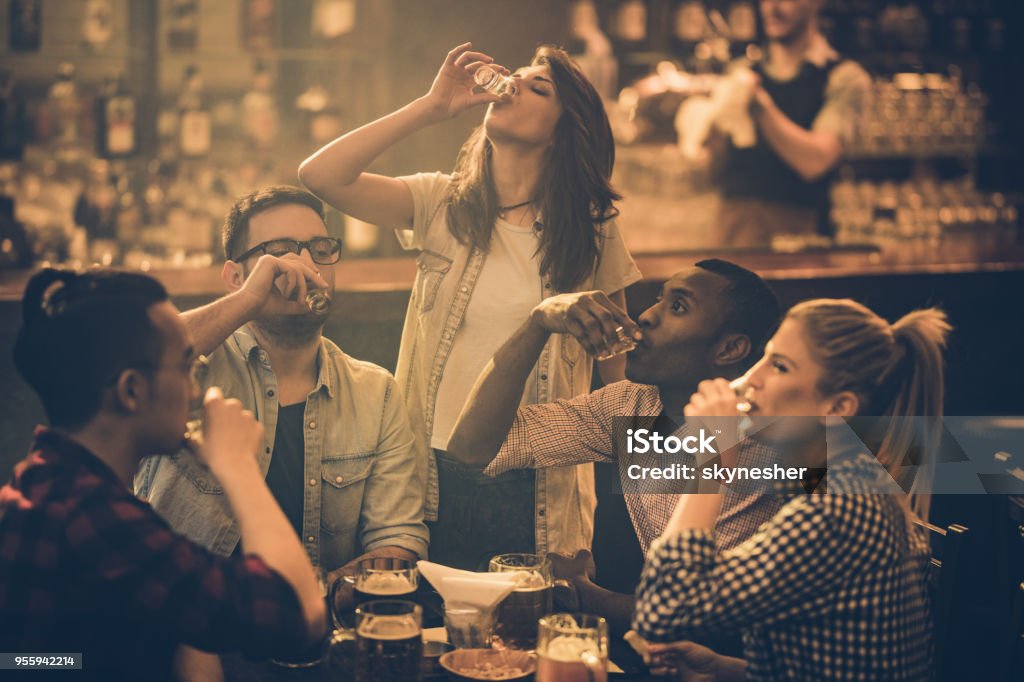 Group of young friends drinking tequila shots in a bar. Young friends drinking shots while spending their night out in a bar. Shot Glass Stock Photo
