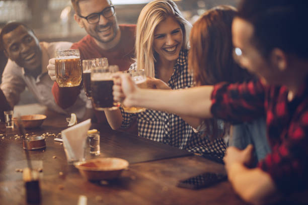 Group of young joyful friends having fun while toasting with beer in a pub.