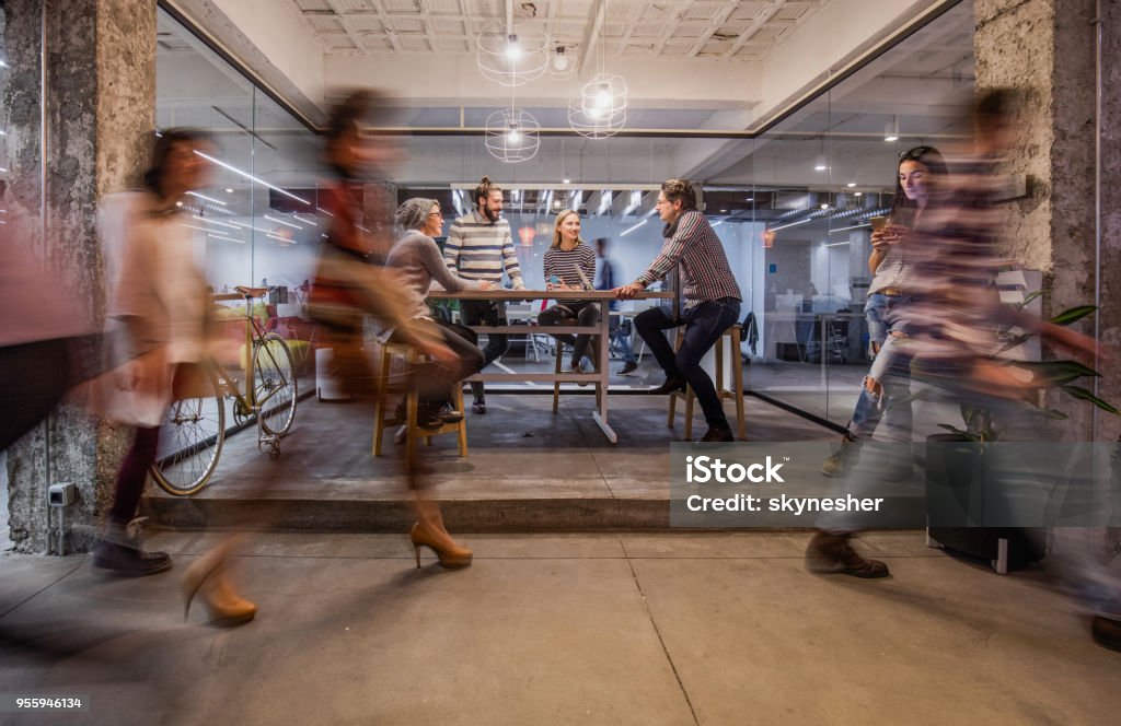 Business meeting at busy corporate office! Happy entrepreneur having a business meeting inside of an office while their colleagues are walking in blurred motion. Office Stock Photo