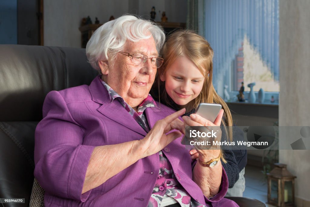Nenek menunjukkan cucunya sesuatu yang lucu di smartphone-nya - Bebas Royalti Perempuan lansia - Perempuan dewasa Foto Stok