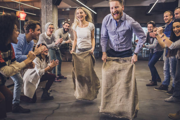 Carefree freelancers having fun during a sack race at casual office. Large group of happy entrepreneurs having fun on a sack race in the office, race office stock pictures, royalty-free photos & images