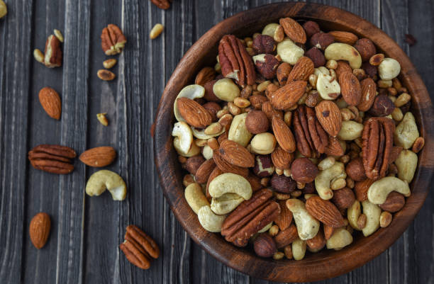 istock Nuts mix Almonds, Cashews, Macadamia, Peanuts, Walnuts, Pecans, Pine Nuts, Pistachios in a wooden plate 955948712