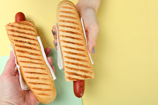 Two French hot dogs in hands against a background of pastel colors. Top view.