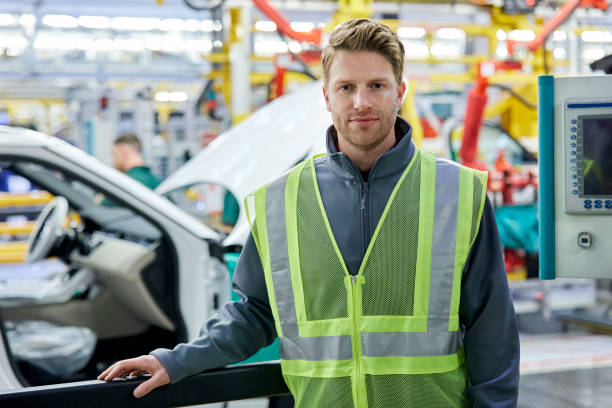 Confident male engineers standing in car plant Portrait of engineer standing in automobile industry. Confident professional is standing in car plant. Male is wearing reflective clothing at factory. car portrait men expertise stock pictures, royalty-free photos & images