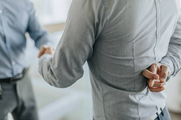 Dishonesty in closing the deal! Close up of unrecognizable businessman holding his fingers crossed while shaking hands with his colleague. fingers crossed stock pictures, royalty-free photos & images