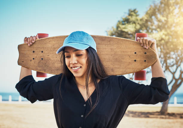 Lovely young woman with her skateboard at the seaside Young urban beauty holds her skateboard by the sea. woman wearing baseball cap stock pictures, royalty-free photos & images