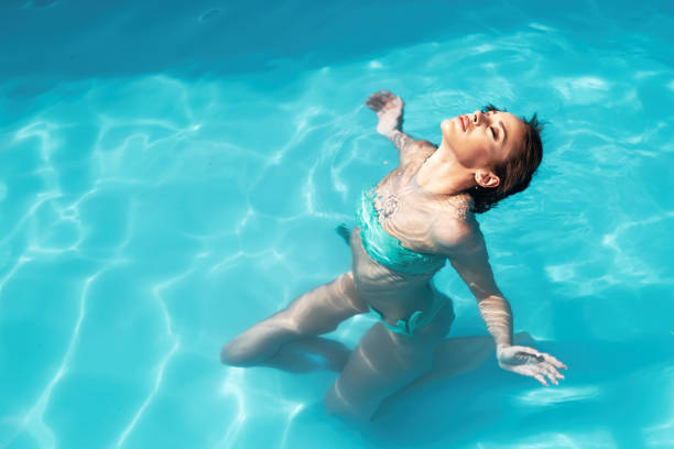 Beautiful teenage girl enjoying water for a portrait in pool backyard on a very sunny summer day. She has long hair and is wearing a swimsuit. Horizontal waist up outdoors shot with copy space.