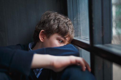 Adolescente muchacho triste pensativo en una camisa azul y pantalones vaqueros sentados en la ventana y se cierra su rostro con sus manos. photo