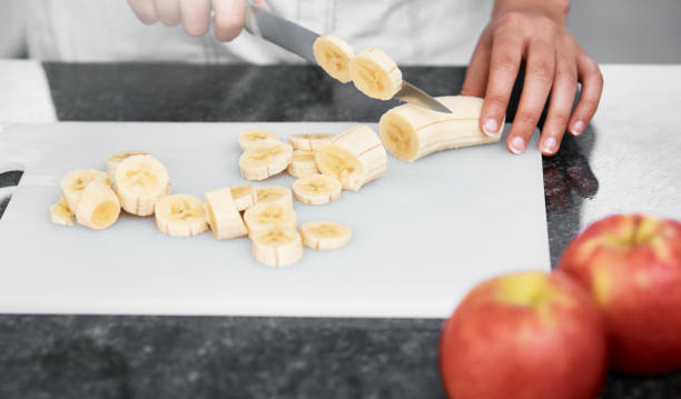 istock Female hands slicing bananas, other fruit alongside 955994152