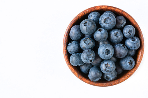 Fresh blueberries in wooden bowl on white background. Top view, copy space for text. Isolated