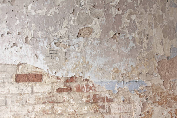 istock Old flaky white paint peeling off a grungy cracked wall. Cracks, scrapes, peeling old paint and plaster on background of old cement wall. An old cement stone wall as vintage cracked. Brick wall. 955999770