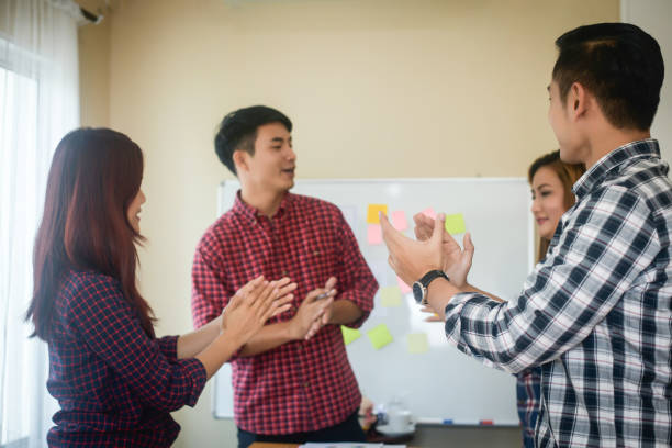 istock Handsome young man standing near whiteboard and pointing on the chart presentation perfect planning business with people group clapping. 956004676