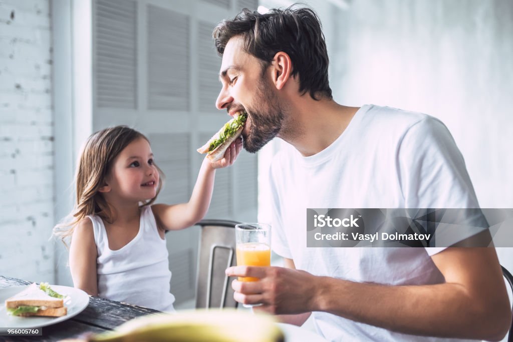 Dad with daughter at home I love you, dad! Handsome young man at home with his little cute girl are having breakfast. Happy Father's Day! Eating Stock Photo