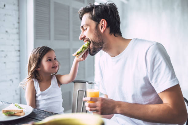 Dad with daughter at home I love you, dad! Handsome young man at home with his little cute girl are having breakfast. Happy Father's Day! eating stock pictures, royalty-free photos & images