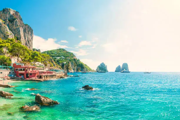 view of faraglioni rocks at sunset from Marina Piccola beach on summer day with turquoise blue waters and beachfront cafes, Capri, Italy