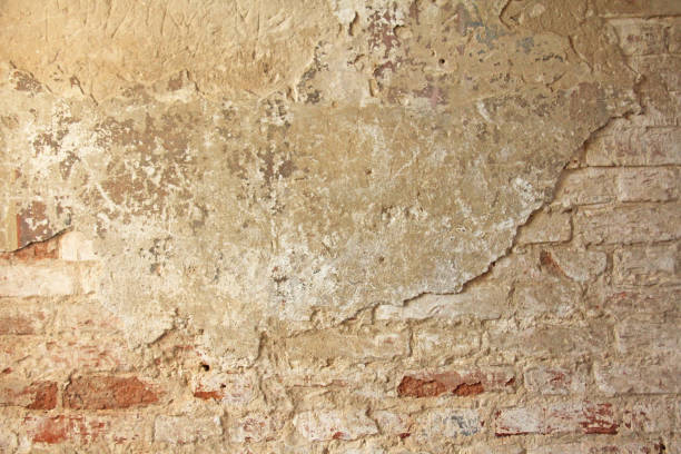 istock Old flaky white paint peeling off a grungy cracked wall. Cracks, scrapes, peeling old paint and plaster on background of old cement wall. An old cement stone wall as vintage cracked. Brick wall. 956014444