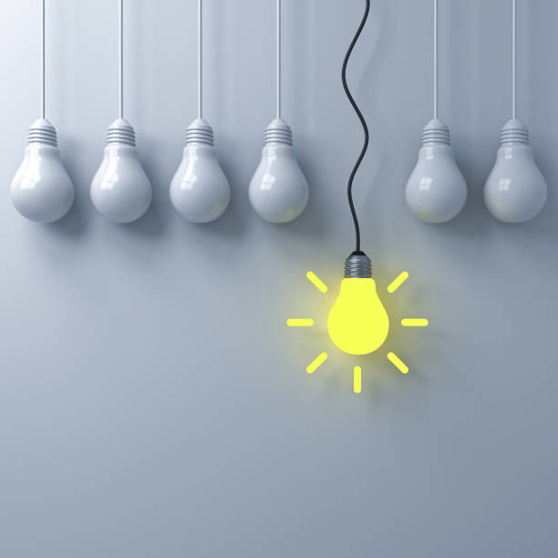 istock Think different concept , One hanging glowing light bulb standing out from the dim unlit light bulbs on white wall background , leadership and individuality creative idea concepts . 3D rendering 956014610