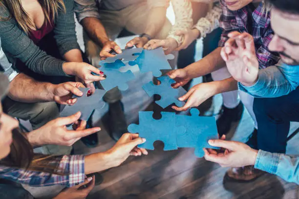 Businesspeople joining puzzle pieces in office, close up.