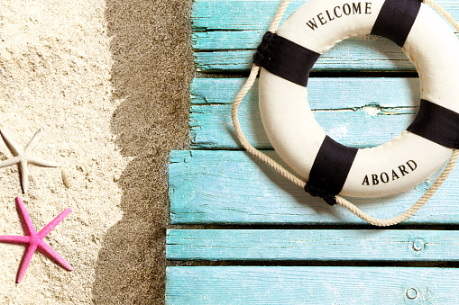 Summer background. Life buoy and sea life on sand and blue wooden boards, on the beach. Horizontal orientation.