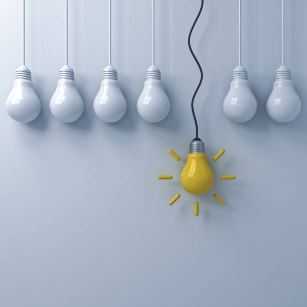 istock One hanging yellow idea bulb standing out from the dim unlit light bulbs on white wall background , Think different and individuality creative idea concepts . 3D rendering 956017284