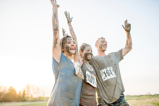 Two women and a man are doing a mud run together. They are covered in dried mud. They are cheering after finishing the race.