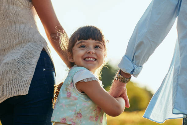 Some call them parents, I call them guardian angels Portrait of an adorable and happy little girl holding her mother and father’s hands in the park kid holding fathers hand stock pictures, royalty-free photos & images