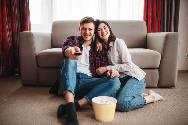 istock Couple sitting on floor and watch tv with popcorn 956027162