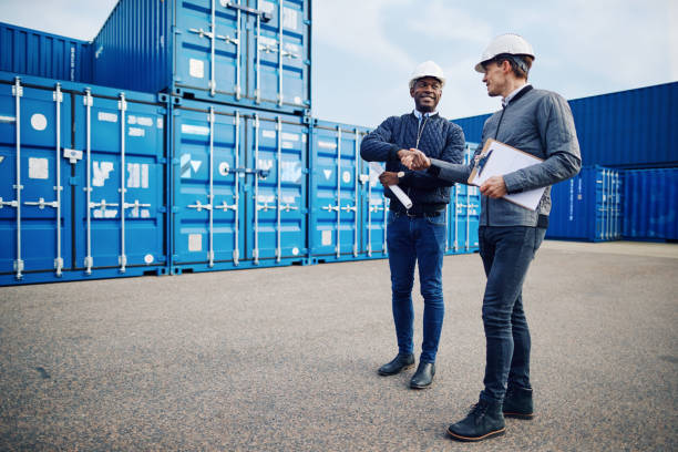 istock Smiling engineers shaking hands together in a shipping yard 956031816