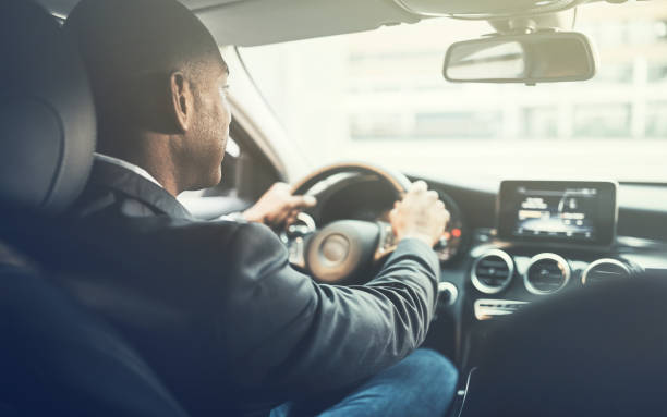 Young African man driving a car through the city Rearview of a young African businessman driving through the city streets in his car black taxi stock pictures, royalty-free photos & images