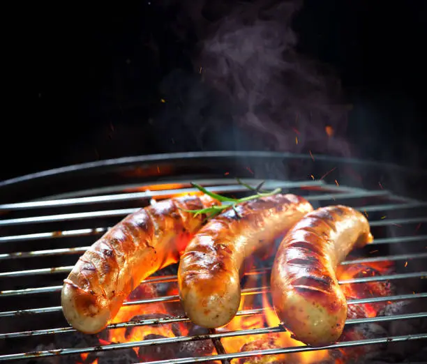 Grilled sausages on grill with smoke and flame on dark background