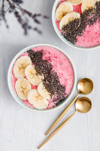 Top view of summer smoothie bowls with strawberry, banana and chia seeds over white background. The concept of vegan and healthy food.