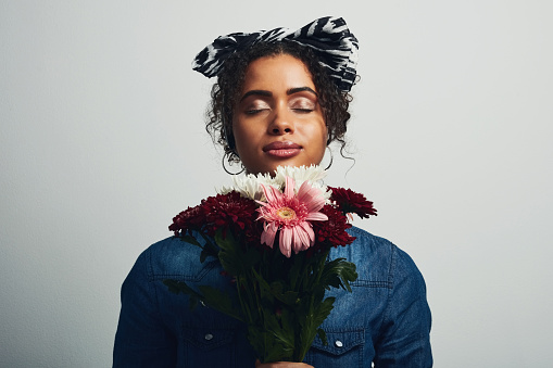 Studio shot of an attractive young woman holding a bunch of flowers against a grey background