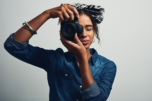 Studio shot of an attractive young woman taking a picture with a dslr camera against a grey background