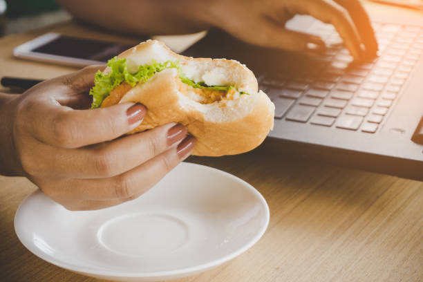 istock woman eating junk food burger  while working on computer laptop 956066784
