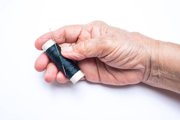 Senior woman's hands holding thread roll with needle isolated on white background, About tailor