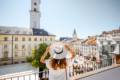 Young woman tourist enjoying great view on the old town with town hall tower in Lviv city during the sunny weather in Ukraine