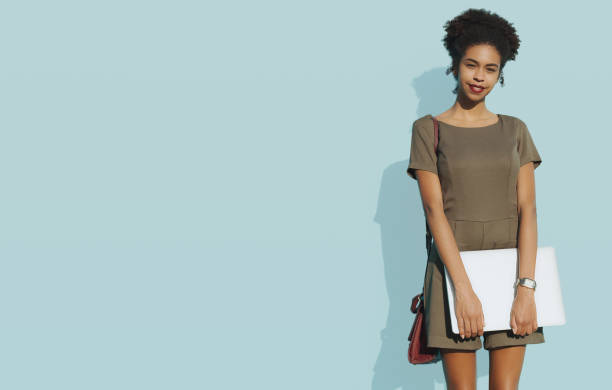 African-American female with laptop next to solid blue wall Young cheerful Brazilian female student in front of a bluish wall holding a closed laptop; cute African-American girl with curly hair and the netbook on a solid background filled with the teal color solid colour stock pictures, royalty-free photos & images