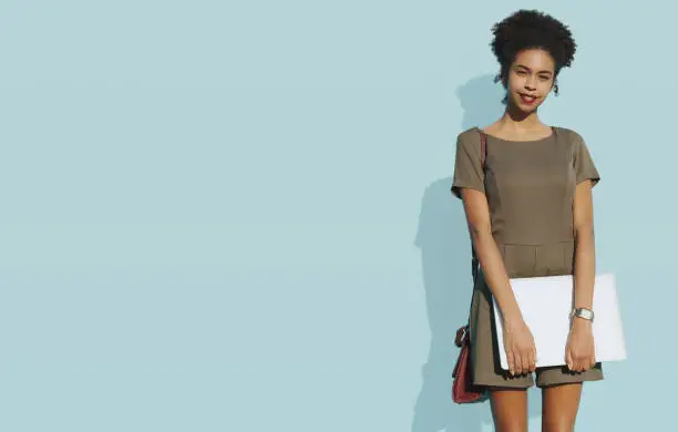 Photo of African-American female with laptop next to solid blue wall