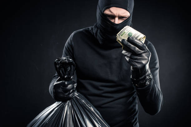 istock Man in balaclava holding plastic bag with cash and dollars 956077314