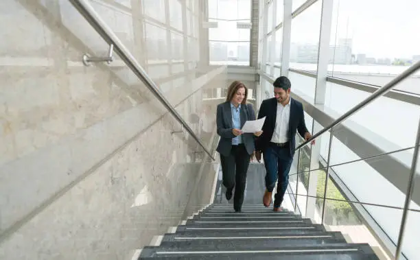 Business partners walking up the stairs to the office looking at a document very satisfied and happy
