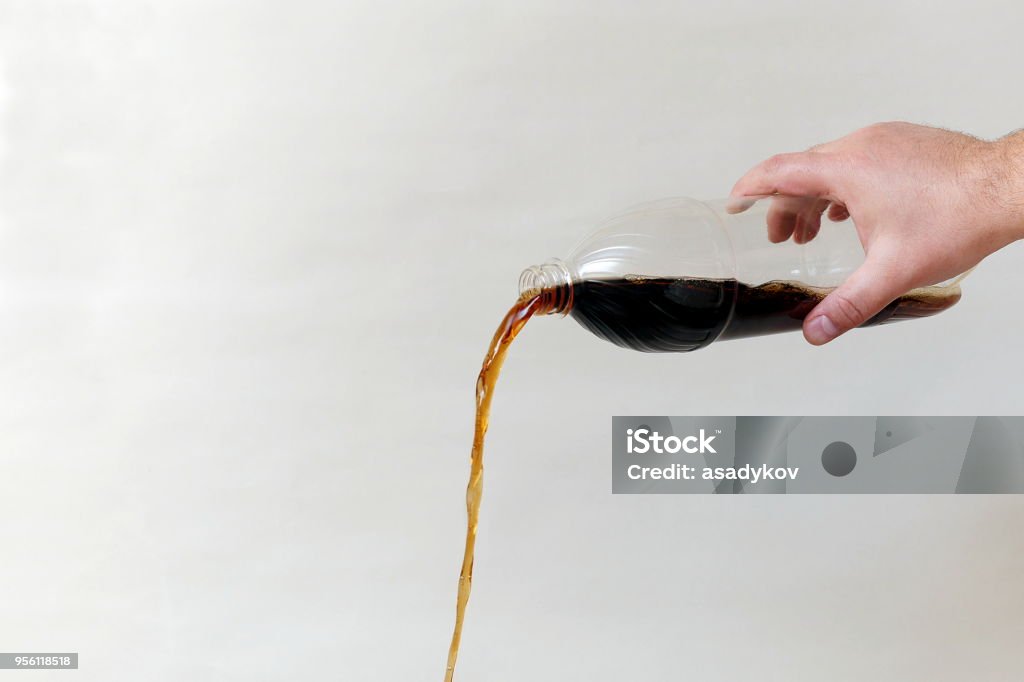 hand pouring out cola from plastic bottle on gray background, copy space Cola Stock Photo