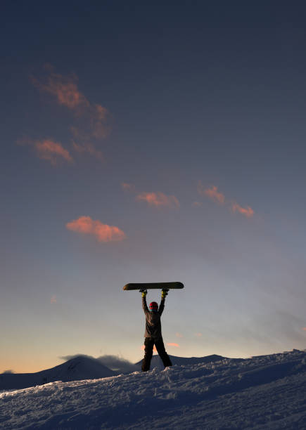 Girl raises snowboard up against  dark sunset sky Girl raises snowboard up against the dark sunset sky ski resort flash stock pictures, royalty-free photos & images